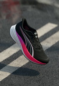 Μαύρο αθλητικό παπούτσι με υφή στην επάνω επιφάνεια, έντονες ροζ και λευκές λεπτομέρειες, και ελαφριά σόλα με δυναμικά σχεδιαστικά στοιχεία.