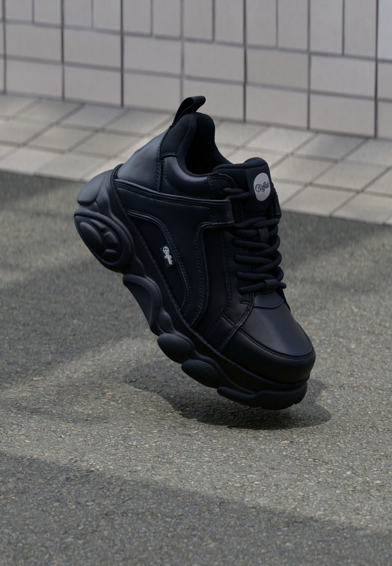 Zapatilla negra con suela gruesa, parte superior de piel suave y acentos texturizados. Presenta una puntera redonda y costuras decorativas.