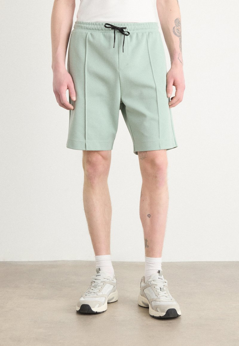 Shorts vert menthe en tissu doux avec une taille élastique et un cordon de serrage ; dotés de plis latéraux et se situant au-dessus du genou.