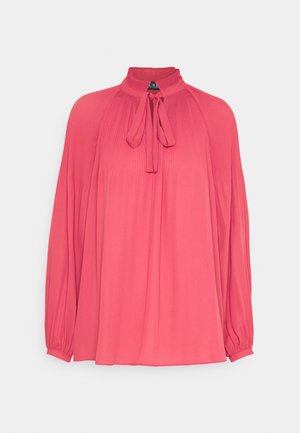 Koralfarvet pink bluse med lange ærmer, plisserede skuldre og ærmer, høj flæset krave og bindebånd foran ved halsudskæringen.