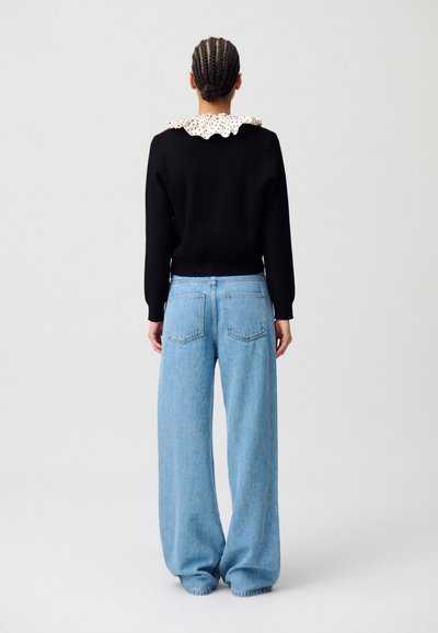 Suéter negro con un cuello blanco de volantes y lunares, combinado con jeans de pierna ancha de color azul claro que cuentan con bolsillos traseros y una cintura alta.