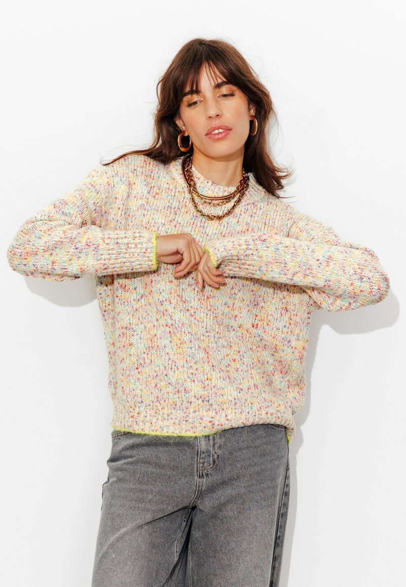 Pull en tricot avec fil moucheté multicolore, col rond côtelé et manches longues, porté avec un jean gris. Manches avec poignets contrastants.