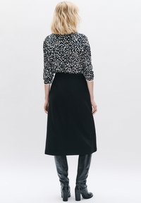 Gonna nera midi con vita aderente, abbinata a una blusa a maniche lunghe a motivi nei toni del nero e del crema. Stivali neri in pelle fino al ginocchio.