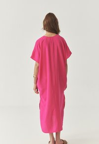 Rosa, oversized kjole med korte ærmer, lavet af et let materiale. Har sideslids og en afrundet halsudskæring, hvilket giver en afslappet pasform.