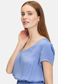 Haut à manches courtes, bleu clair, avec un décolleté en V, fabriqué en tissu doux avec une texture lisse et un léger tombé.