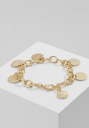Bracelet chaîne en or avec six breloques rondes et plates espacées uniformément, une breloque gravée du nom de la marque, exposé sur un socle blanc.
