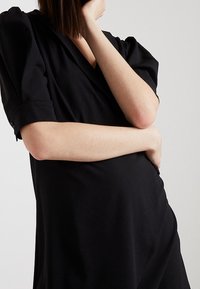 Black wrap dress with short, puffed sleeves, soft fabric, and a V-neck design, featuring a loose fit and a knee-length hemline.