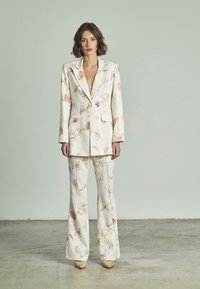 Conjunto de estampado floral en suave tejido crema, con una chaqueta estructurada y pantalones acampanados. Notables acentos en rosa y verde a lo largo del diseño.