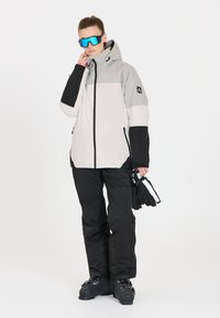 Ski jakke i grå og sort med hætte, parret med sorte skibukser og handsker, med et elegant design og atletisk pasform.