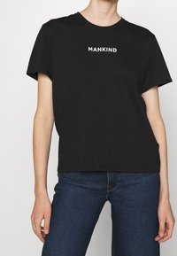 Černé bavlněné tričko s krátkým rukávem a kulatým výstřihem, s bílým nápisem "MANKIND" ve středu na přední straně.