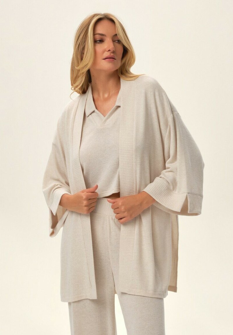 Kremowy sweter dzianinowy z szerokimi rękawami, teksturowanym dołem i pasującym zestawem pod spodem. Miękka, lekka tkanina. Swobodna odzież do wypoczynku.