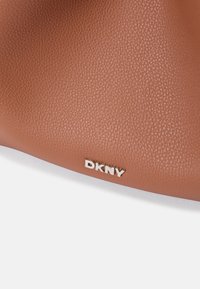 Geantă din piele texturată maro cu un logo metallic DKNY. Suprafața are un finisaj cu granulație, adăugând adâncime și detaliu.
