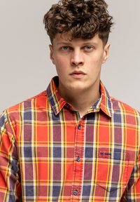 Koszula w kratę w czerwono-żółto-niebieskim wzorze, wykonana z bawełny, z zapinanym kołnierzykiem i kieszenią na piersi z detalem logo.