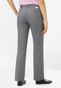 Pantaloni grigi con vita aderente, design a gamba dritta e texture sottile. Comprendono una tasca posteriore e sono indossati con delle ballerine nere.