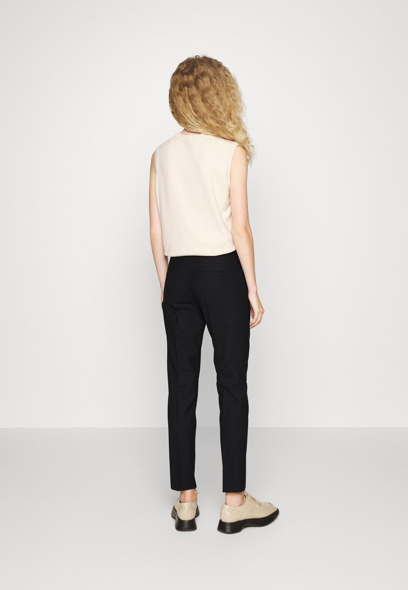 Ärmelloses hellbeiges Top, kombiniert mit schwarzen, taillierten Hosen, die eine glatte Textur und ein minimalistisches Design aufweisen. Beigefarbene Schuhe mit einer klobigen Sohle.