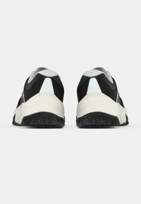 Fekete-fehér sportcipőpár hátulnézetben, texturált fekete talpakkal és fehér sarokdíszítéssel, fehér háttéren.