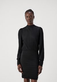 Robe noire à design plissé, avec manches longues, col haut et silhouette ajustée. Texture lisse tout au long.