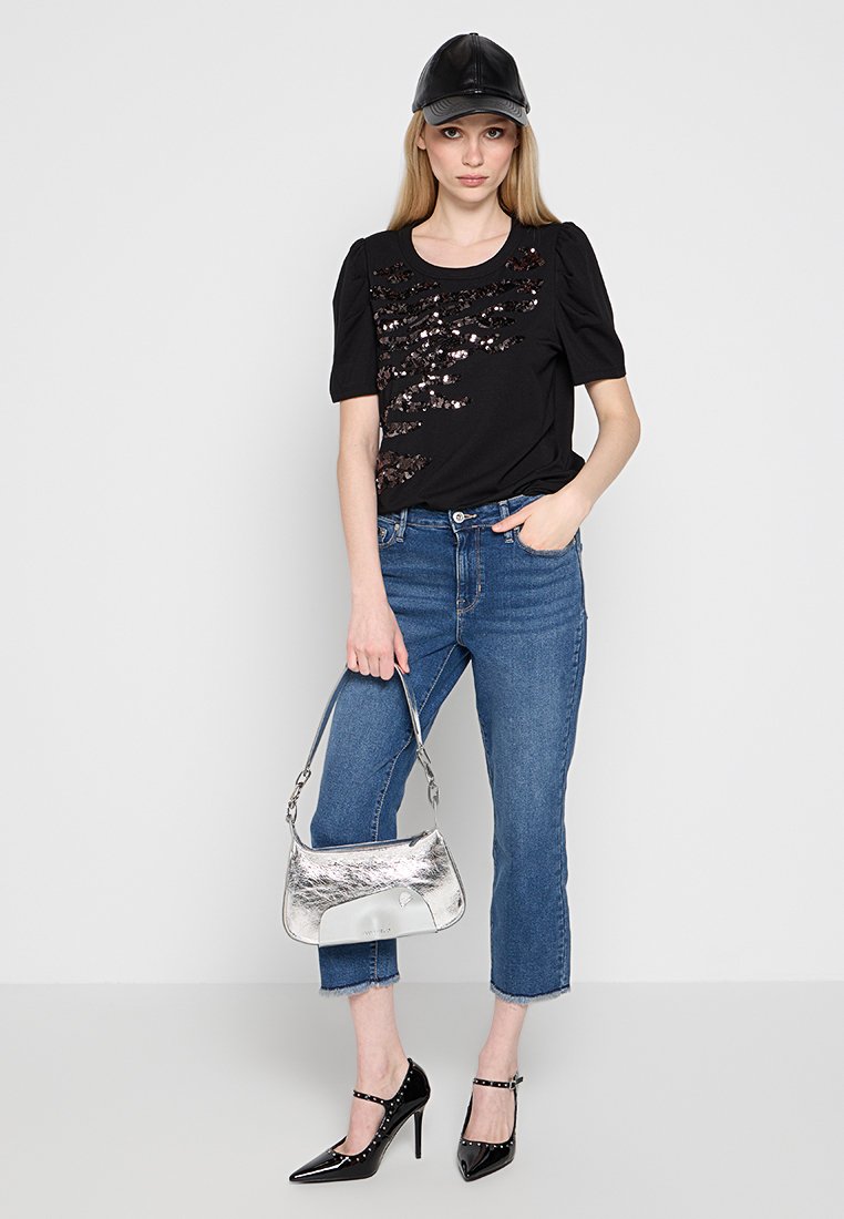T-shirt nera con design di paillettes, jeans blu a vita alta, borsa argento e tacchi neri in vernice. Un berretto di pelle completa l'outfit.