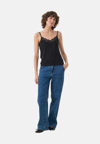 Black camisole with lace trim at the neckline, paired with high-waisted blue denim flared jeans. Model stands with one hand in pocket.