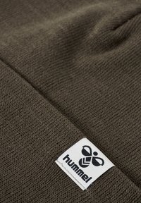 Bruine gebreide beanie muts met een ribbel structuur. Bevat een geweven wit etiket met een logo en merknaam aan de voorkant.