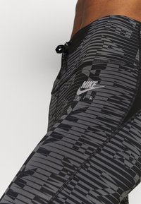 Svarta leggings med ett strukturerat grått geometriskt mönster, med en Nike-logga och en justerbar dragsko i midjan.