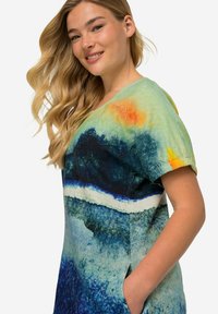 Mehrfarbiges Kleid mit einem grünen Oberteil, einem blau-weißen Wellenmuster, kurzen Ärmeln und Seitentaschen, aus weichem Stoff gefertigt.