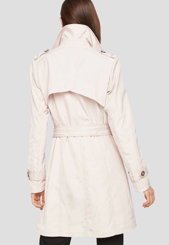 Femme portant un trench-coat beige clair avec ceinture et rabat coupe-vent, vue de dos sur un fond uni.