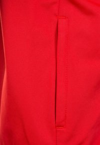 Rode stof met een gladde textuur heeft een verticale uitsnijding. Stiksel is zichtbaar in een contrasterende kleur langs de randen.