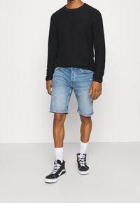 Black ribbed long-sleeve shirt, light blue distressed denim shorts, white socks, and black sneakers with white accents.