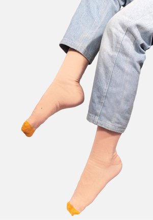 Jasnoróżowe skarpetki z żółtymi noskami, wykonane z bawełny, widoczne powyżej kostki, zestawione z podwiniętymi jasnoniebieskimi dżinsami. Gładka tekstura.