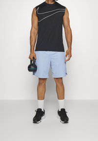 Débardeur de sport noir avec un motif blanc, short bleu clair et kettlebell noir. Baskets noires avec semelles blanches et chaussettes montantes.