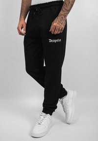 Juodos sportinės kelnės su elastingu juosmeniu ir raišteliu. Virš dešinės šlaunies yra baltas "Dropsize" logotipas. Derinamos su baltais sportbačiais.