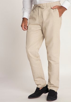 Pantalones beige, ligeros, con cordón en la cintura, bolsillos laterales y un corte relajado, combinados con mocasines de ante negros. Textura y diseño sencillos.