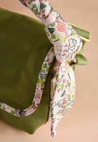 Borsa di stoffa verde con manico in tessuto a fantasia floreale annodato a fiocco, con dettagli rosa e verdi e hardware dorato.