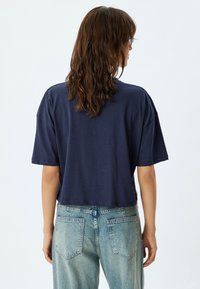 Camiseta recortada azul marino de manga corta, con un ajuste relajado y textura suave, combinada con jeans de denim claro con bolsillos traseros.