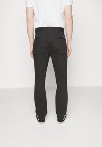 Pantaloni neri con taglio dritto, realizzati in un tessuto morbido. Presentano una vita alta e due tasche posteriori. Indossati con sneakers nere.