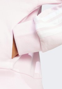 Lys rosa sweatshirt med en glatt tekstur, med en sidelomme og hvite stripete detaljer på ermene. Enkelt design og avslappet passform.