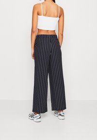 Marintröjor med vida ben, vita vertikala ränder, elastisk midja och sidofickor, kombinerat med en vit kort topp och sneakers.