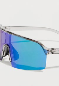Lunettes de soleil à monture transparente et large verre incurvé dégradé du violet au bleu. Caractérisées par un design audacieux et angulaire avec des accents chromés.
