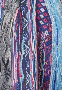 Colorful woven fabric featuring interlacing patterns of blue, pink, black, and white, with a textured finish and geometric designs.