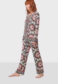 Conjunto de pijama de dos piezas en color crema, con un atrevido patrón circular en rojo y negro. Tejido suave, mangas largas y pantalones de corte relajado.