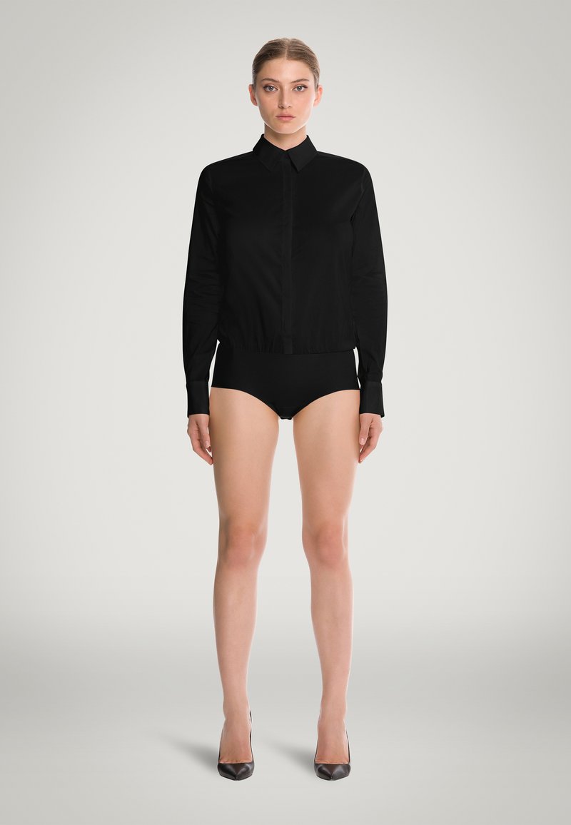 Svart långärmad skjorta med slim fit och rak krage, tillverkad av ett mjukt tyg, tillsammans med svarta underkläder och spetsiga klackar.