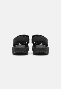 Mustad mustad, millel on reguleeritavad rihmad, tasane tall, tekstureeritud kummi välistald ja minimalistlik disain; sobib igapäevaseks kandmiseks.