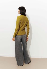 Pull en tricot côtelé jaune moutarde avec un col haut, associé à un jean gris délavé à jambes larges. Texture lisse et coupe décontractée.