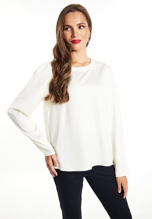 Weißes Langarmbluse mit rundem Ausschnitt und weichem Material, kombiniert mit schwarzen Hosen. Verfügt über leichte Schulterfalten für zusätzlichen Detail.