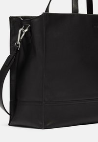 Schwarze Leder-Umhängetasche mit vertikalen Nähten, doppelten Griffen und einem abnehmbaren Schultergurt. Verfügt über silberfarbene Beschläge und eine strukturierte Oberfläche.