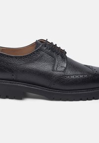 Scarpa da uomo in pelle nera con superficie texture, punta tonda, allacciatura tradizionale e suola nera resistente progettata per la trazione.