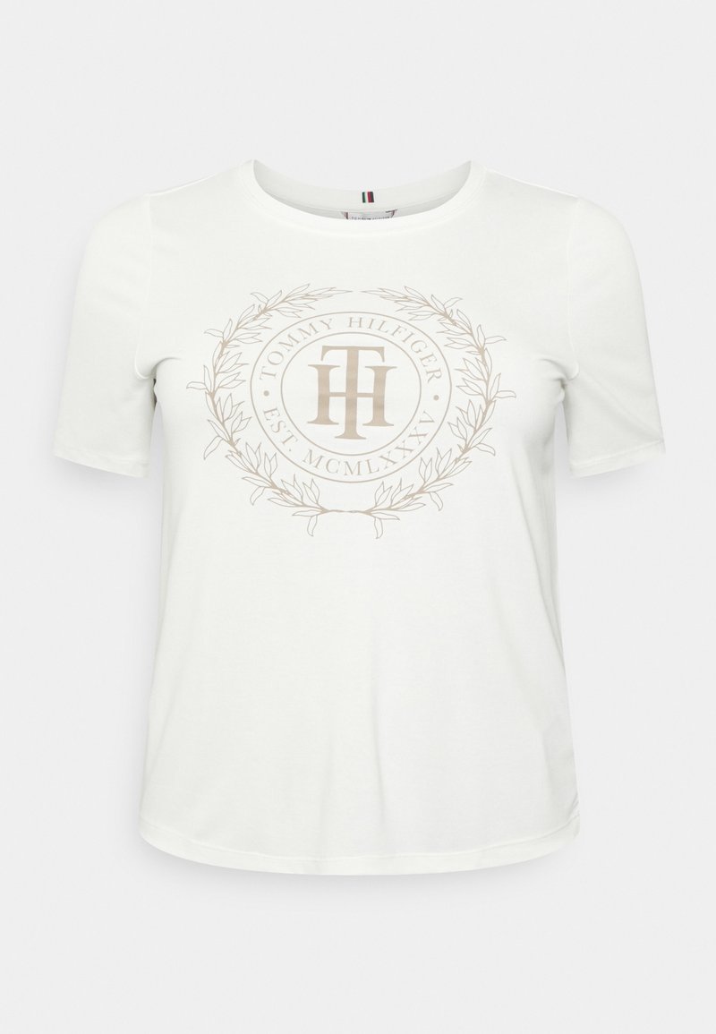 White cotton t-shirt with short sleeves, featuring a beige circular logo with "Tommy Hilfiger" and laurel design in the center.