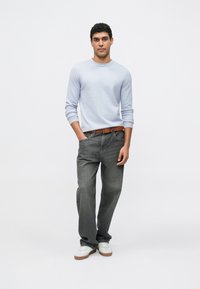 Lichtblauw shirt met lange mouwen, grijze jeans met rechte pijpen, bruine riem en witte sneakers met bruine zolen; casual outfit met een ontspannen pasvorm.