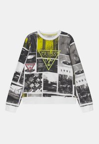 Sudadera blanca con un collage de imágenes en blanco y negro, con acentos en verde y amarillo, logotipos de GUESS y un cuello acanalado.